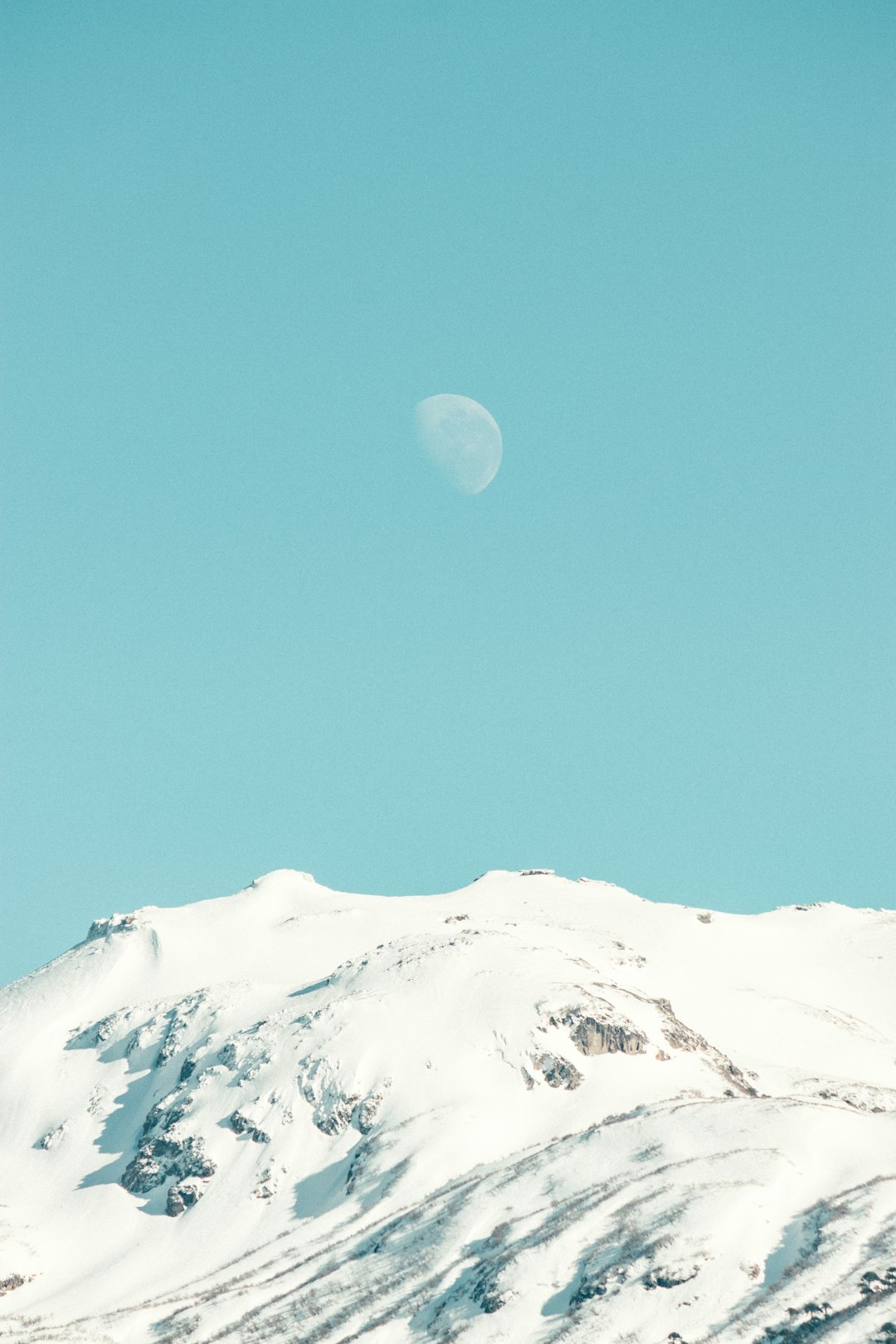 A snow covered mountain with a half moon in the sky